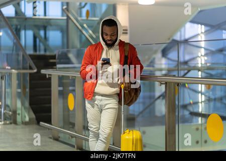 Young African man traveler with baggage surfing internet or connecting to free airport wifi Stock Photo