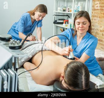 Cosmetologists performing hardware body procedure for young woman Stock Photo