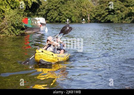 A woman and a man paddle a yellow inflatable kayak along the River Thames on a bright sunny day Stock Photo