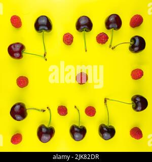 Lines of  dark red cherries with green stems and red and pink raspberries on a yellow field. Stock Photo
