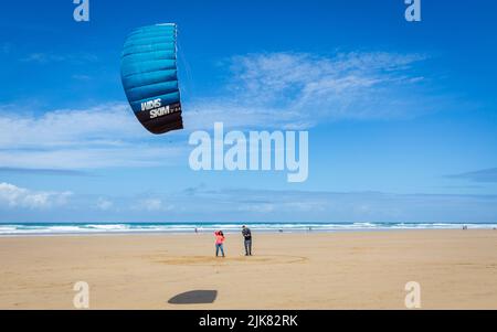 Beach kite board kite training. A man teaches his girlfriend how to fly a power kite on a sunny, windy summer day on a beautiful beach in Cornwall Stock Photo
