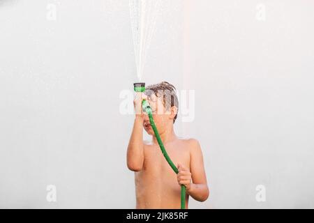 Child playing with a hose to cool off with water during a summer heat wave in Europe. Stock Photo