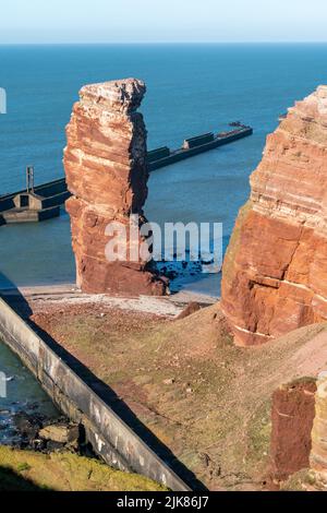 Lange Anna sea stack and tall red dramatic cliffs of Heligoland island on a nice sunny day in the North sea, Germany. Famous rock tower. Blue waters Stock Photo