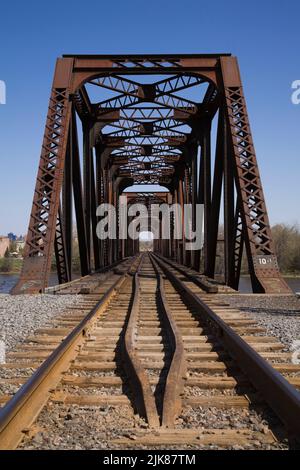 Railroad tracks leading to old rusted Terrebonne rivet connected Pratt truss railway bridge, Laval, Quebec, Canada. Stock Photo