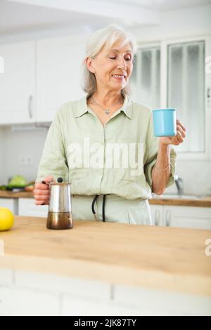Cheerful senior woman having breakfast with cup of coffee Stock Photo