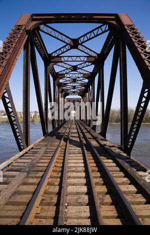 Railroad tracks leading to old rusted Terrebonne rivet connected Pratt truss railway bridge, Laval, Quebec, Canada. Stock Photo
