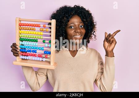 Young african american woman holding traditional abacus smiling happy pointing with hand and finger to the side Stock Photo