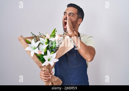Hispanic man with beard working as florist shouting and screaming loud to side with hand on mouth. communication concept. Stock Photo
