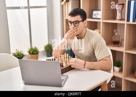Young arab man playing chess online covering mouth with hand, shocked and afraid for mistake. surprised expression Stock Photo