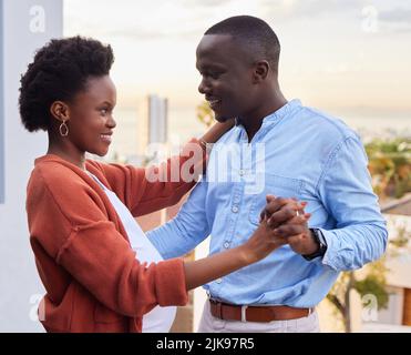 Dancing into this next chapter in life with you. a happy young couple standing together and dancing on their balcony at home. Stock Photo