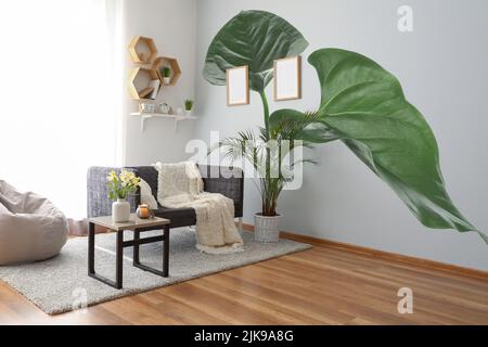 Interior of beautiful light living room with print of monstera leaves on wall Stock Photo