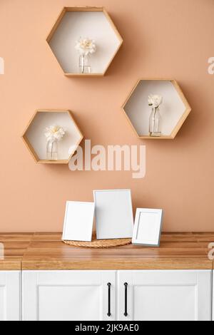 Blank photo frames on kitchen counter and shelves with beautiful peony flowers on beige wall Stock Photo