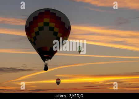 Hot air balloons are silhouetted against the sky at sunset in a composite image. Stock Photo