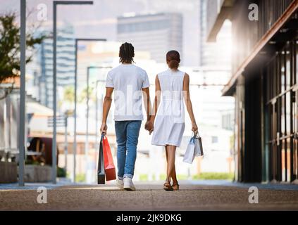 Taking her shopping is always a good idea. a young couple walking hand in hand while holding shopping bags. Stock Photo