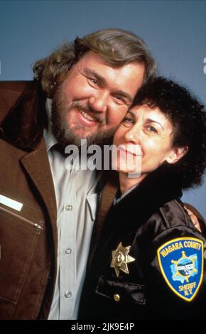 John Candy & Rhea Perlman Film: Canadian Bacon (1996) Characters: Sheriff Bud Boomer, Honey  Director: Michael Moore 08 June 1995   **WARNING** This Photograph is for editorial use only and is the copyright of POLYGRAM VIDEO and/or the Photographer assigned by the Film or Production Company and can only be reproduced by publications in conjunction with the promotion of the above Film. A Mandatory Credit To POLYGRAM VIDEO is required. The Photographer should also be credited when known. No commercial use can be granted without written authority from the Film Company. Stock Photo