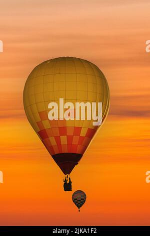 Hot air balloons are silhouetted against the sky at sunset in a composite image. Stock Photo