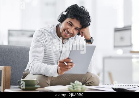His connections allow him to achieve so much more. a young businessman wearing headphones while using a digital tablet in an office. Stock Photo