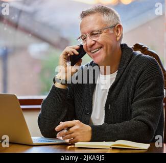 Im happy you called. a handsome senior man making a phonecall while working on his laptop in the study. Stock Photo