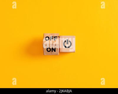 The words on and off on wooden cubes with start icon on yellow background. Power on off switch or start and stop button concept. Stock Photo