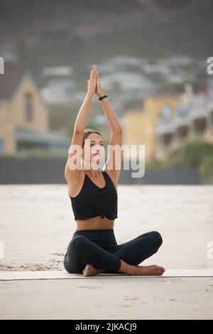 Feel the calm flow through you. a young woman meditating while practising yoga at the beach. Stock Photo