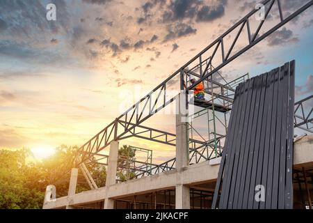 Steel roof truss welders are working on the roof structure with safety devices to prevent fall safety at the construction site. View from the bottom o Stock Photo