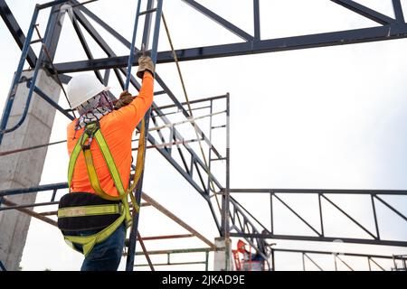 Construction workers are working on steel roof trusses with Fall arrestor device for worker with hooks for safety body harness on the construction sit Stock Photo