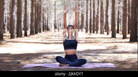 Releasing all that no longer serves me. an attractive young woman sitting alone on a yoga mat outdoors and meditating. Stock Photo