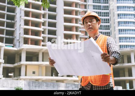 Portrait of architect with blueprint standing in front of building after construction Stock Photo