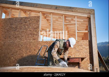 Carpenter using circular saw for cutting wooden OSB board. Man worker building wooden frame house. Carpentry concept. Stock Photo