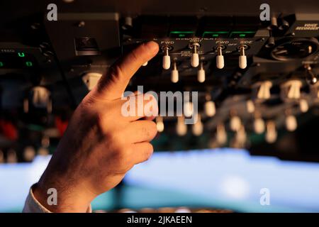 Male captain using control panel in cockpit to fly airborne aircraft, pushing power engine buttons and switch on dashboard command. Using lever and handle with windscreen. Close up. Stock Photo