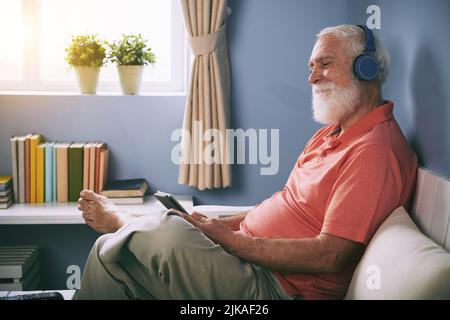 Side view of smiling senior man watching movie on tablet pc at home using wireless headphones Stock Photo