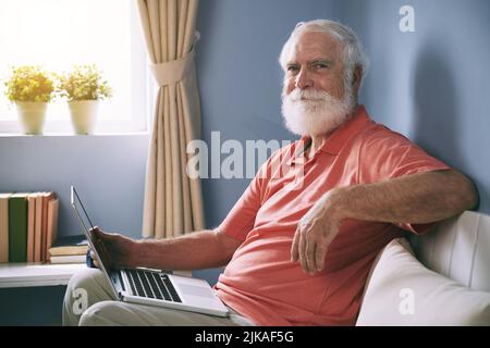 Portrait of handsome elderly man sitting on sofa in domestic room and holding open laptop on his lap Stock Photo