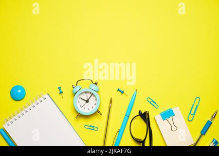 Notebook for writing pen and alarm clock with glasses on yellow background top view, education concept back to school or office supplies Stock Photo