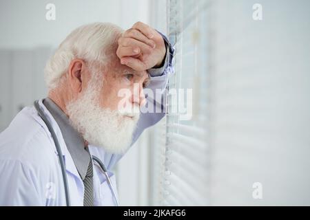 Thoughtful aged general practitioner looking through window in his office Stock Photo