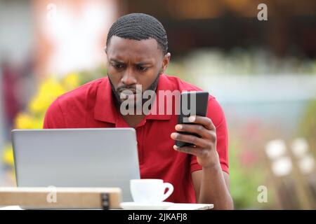 Worried black man in red using multiple devices in a bar terrace Stock Photo