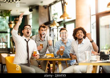 Friends cheering. Four happy soccer fans drinking beer at the pub Stock Photo