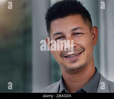 Working overtime wont steal my smile. a handsome young businessman standing alone in the office during a late shift. Stock Photo