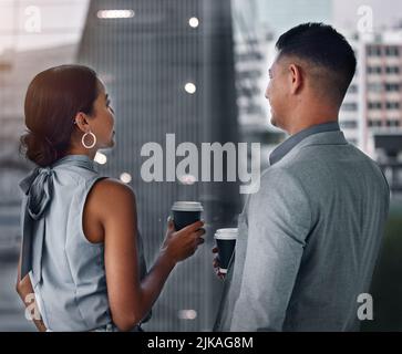 Coworkers and coffee get your through late shifts. two businesspeople standing together in the office and having a discussion in the evening. Stock Photo