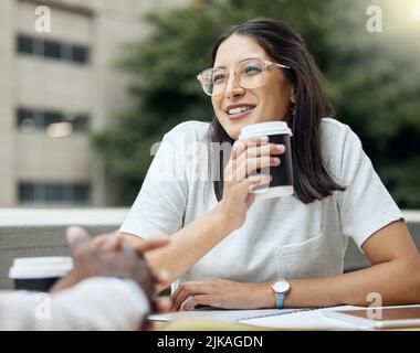 Sharing some light-hearted exchanges with her colleagues over coffee. a young businesswoman having a break with her colleagues outside an office. Stock Photo
