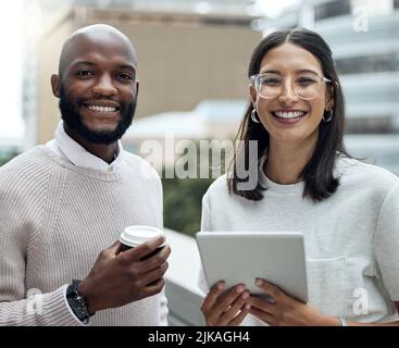 Staying on trend means staying updated. Portrait of two businesspeople drinking coffee and using a digital tablet outside an office. Stock Photo