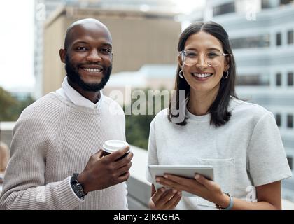 This dynamic duo are always making innovative things happen. Portrait of two businesspeople drinking coffee and using a digital tablet outside an Stock Photo