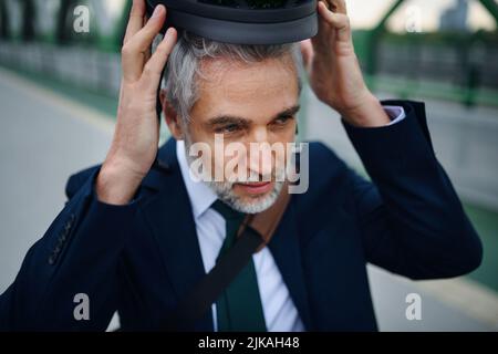 Portrait of businessman commuter on the way to work putting on cycling helmet, sustainable lifestyle concept. Stock Photo