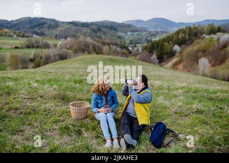Happy young man with Down syndrome with his mother resting in nature, sitting and looking with binoculars. Stock Photo