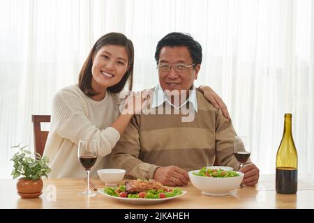 Portrait of happy Vietnamese father and his adult daughter having dinner at home Stock Photo