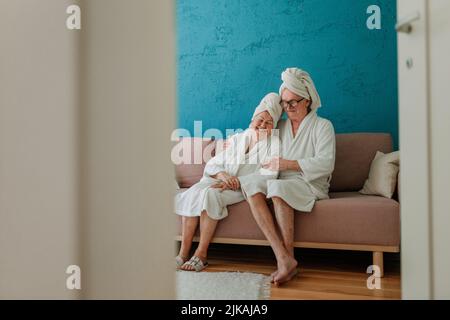 Happy senior couple sitting together in bathrobe on sofa, having nice time at home. Stock Photo