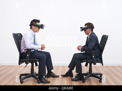 Business people in virtual reality headsets sitting against each other Stock Photo