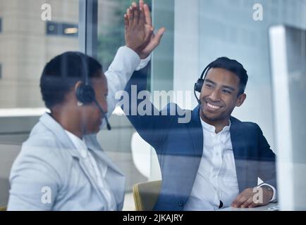 Well done, youre doing great. two young call center agents high fiving while working at their desks in the office. Stock Photo