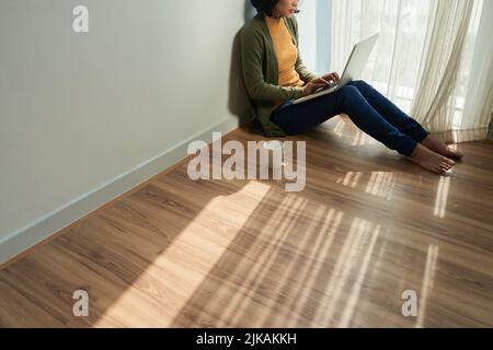 Cropped image of female student sitting on the floor in her room and working on laptop Stock Photo