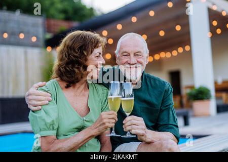 Senior man with his wife celebrating birthday and toasting with wine near backyard pool. Stock Photo