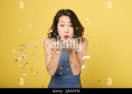 Cheerful young Asian woman blowing confetti into camera Stock Photo